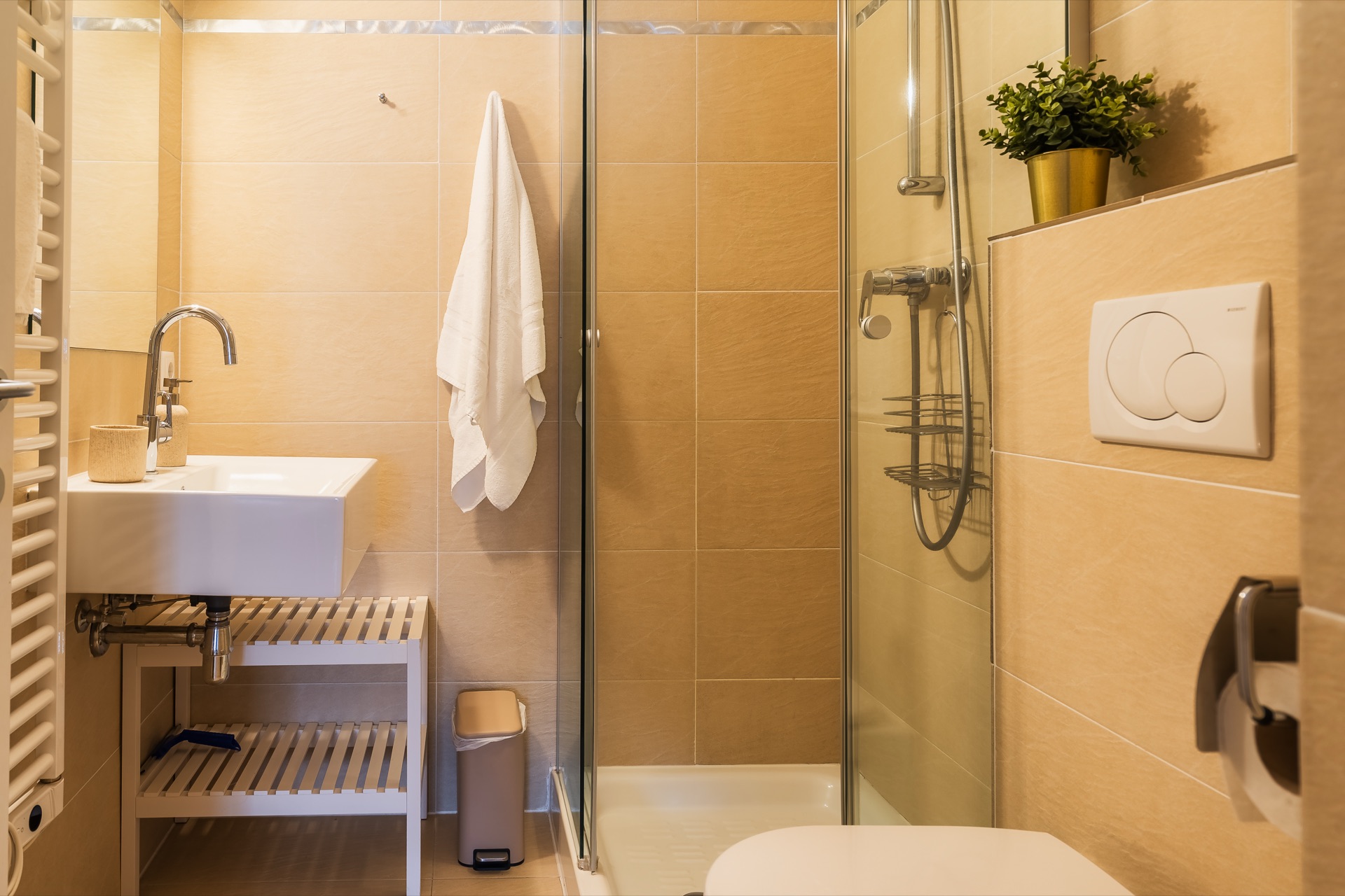 Badezimmer mit ebenerdiger Glasdusche, Waschbecken auf Holzablage, beigen Fliesen, Handtuchheizkörper und kleiner Pflanzendeko beim Alpstay Chalet Nr.1 Bad Kleinkirchheim – Badezimmerfotografie Ferienwohnung Kärnten