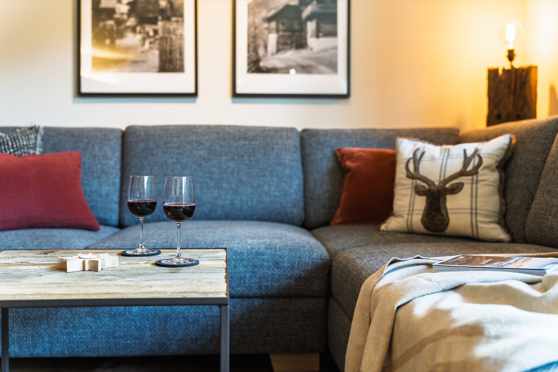 Stimmungsvoller Sofa-Ausschnitt mit zwei Rotwein-Gläsern, Hirsch-Kissen und warmer Abendbeleuchtung in der Fewo Holländer Kärnten – Urlaubsgefühl pur