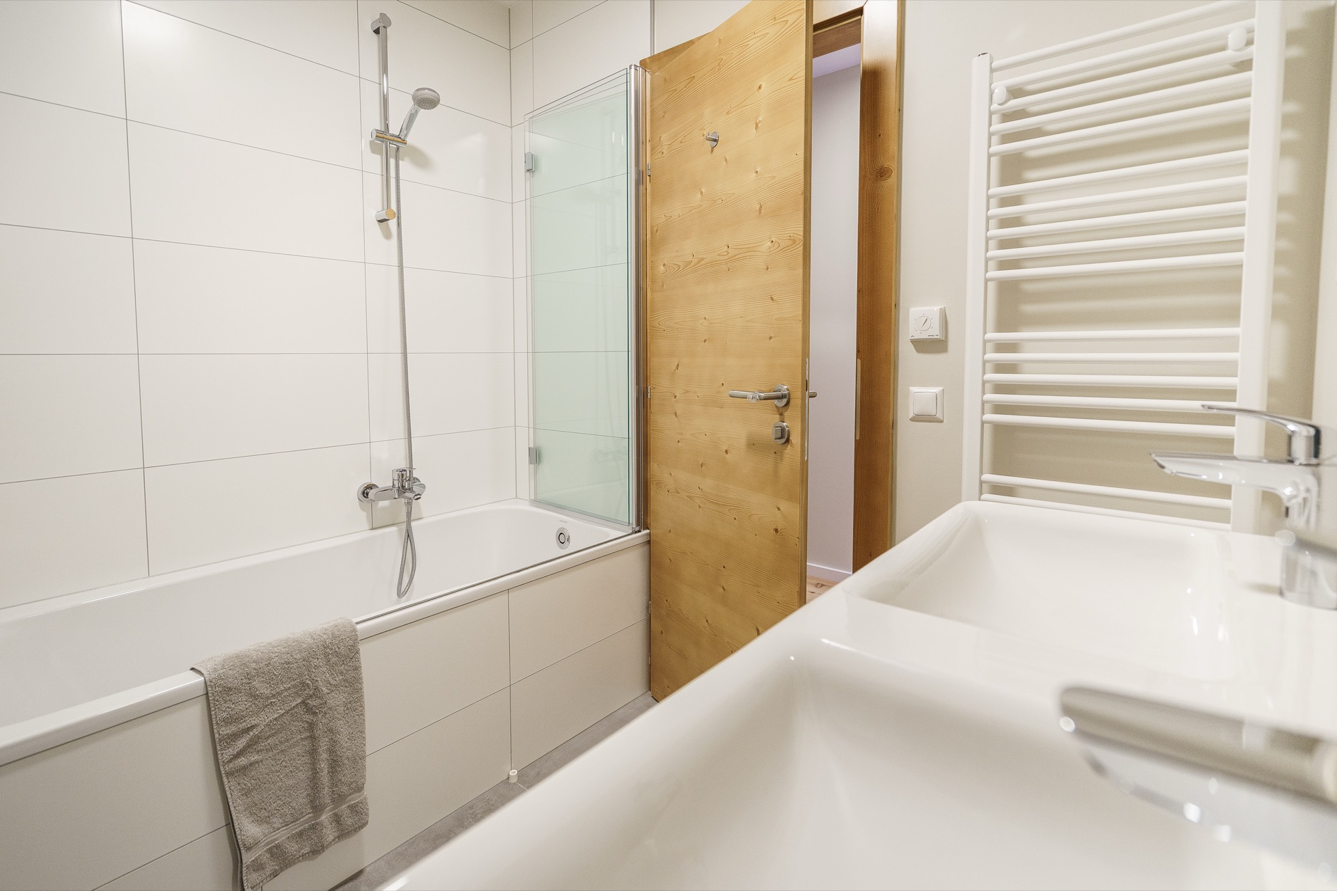 Modernes weißes Badezimmer mit Badewanne, Glasdusche, Doppelwaschbecken und Handtuchheizkörper in der Ferienwohnung Holländer Kärnten – Badezimmerfotografie Ferienwohnung