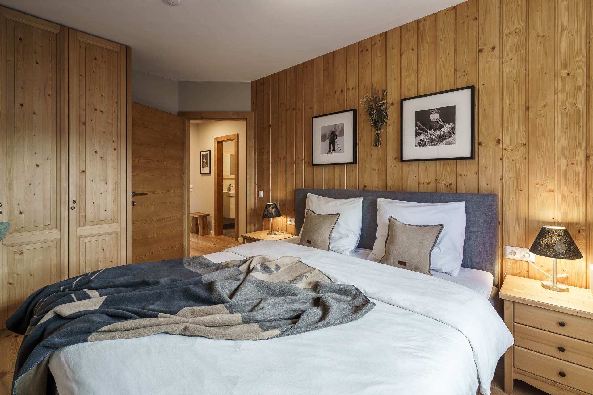 Großzügiges Hauptschlafzimmer mit Zirbenholz-Wandverkleidung, Doppelbett mit Alpindecke, Nachttischlampen und gerahmten Vintage-Skifotos in der Ferienwohnung Holländer Kärnten