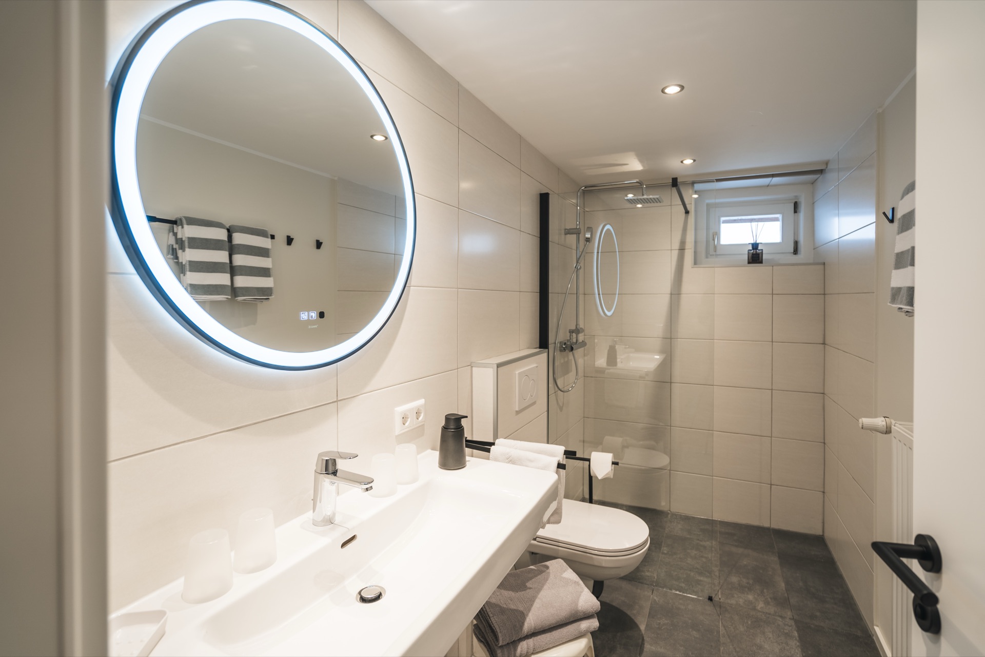 Modernes Badezimmer mit rundem LED-Spiegel, ebenerdiger Dusche und hochwertiger Ausstattung im Landhaus Prägant Bad Kleinkirchheim – Ferienwohnung Fotografie Kärnten